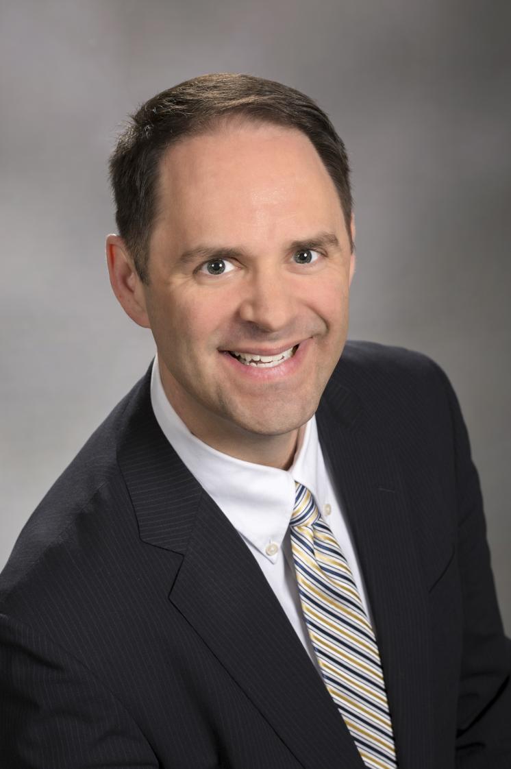 A headshot of a middle-aged man in a black blazer and striped tie.
