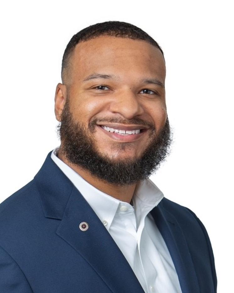 Man with a beard in a dark suit with a white shirt underneath. 