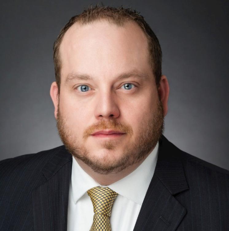 Man with a beard in a dark suit with a white shirt underneath. 