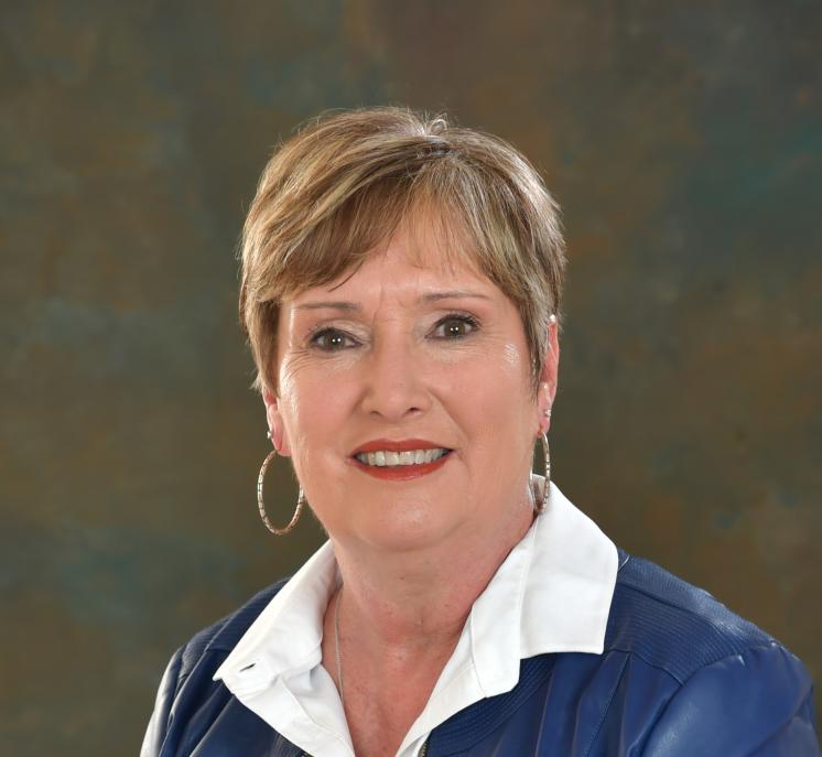A woman standing in a purple shirt with a photographer dark background and studio lighting