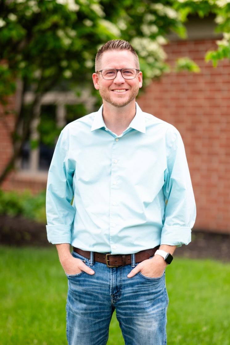 A man standing outside wearing blue jeans and a button down shirt