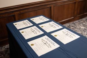 Six certificates on a blue tablecloth against a wooden wall.