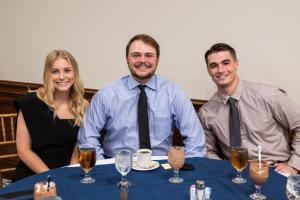 Three people seated at a table with drinks and dishes in a dining setting.