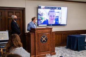A conference room with a podium, a video call on a screen, and presenters.