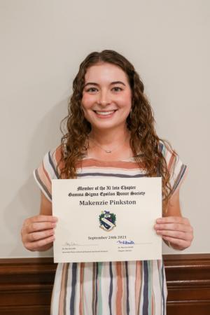 A woman holding a certificate against a white wall with wooden paneling