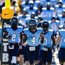 Football players in light blue jerseys running onto the field.