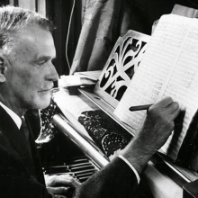Zoltán Kodály writing sheet music on a piano stand
