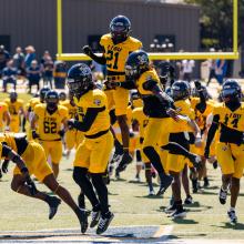 Football players jumping in the air wearing gold uniforms.