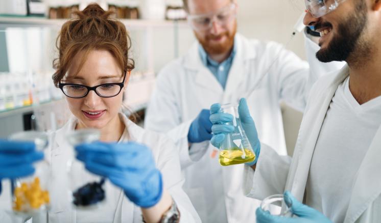 Three researchers in a lab, smiling and holding beakers with substances.