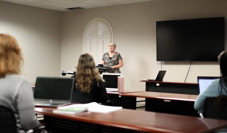 Classroom setting with attendees facing a speaker at a podium.