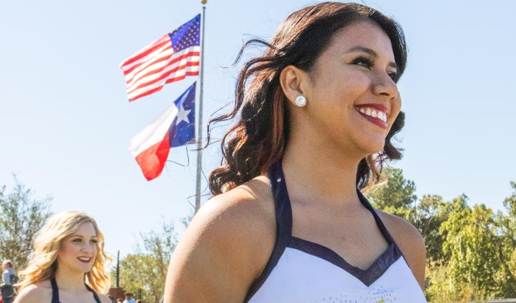 Cheerleader smiling outdoors with flags in the background.