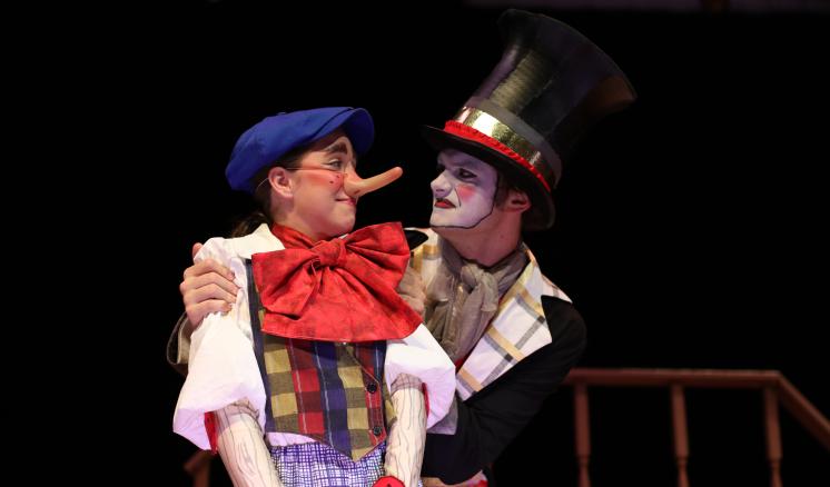 Two performers in theatrical costumes, one dressed as a puppet with a long nose and another in a top hat.