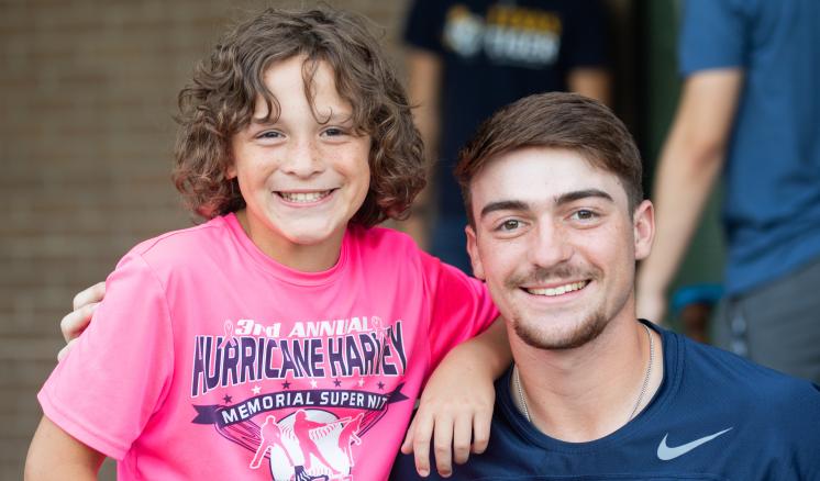 A young person in a pink t-shirt stands next to an adult in a dark shirt, both smiling.