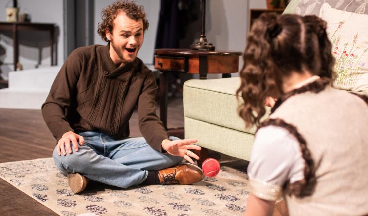 2 actors sitting on the stage of a play talking