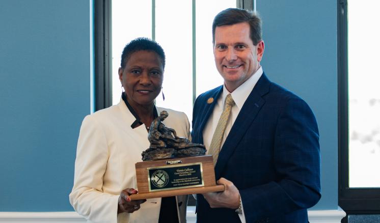 A man and a woman smiling at the camera with an award in between them