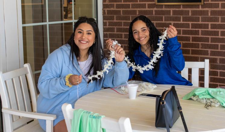 Two women smiling at the camera making flower necklaces