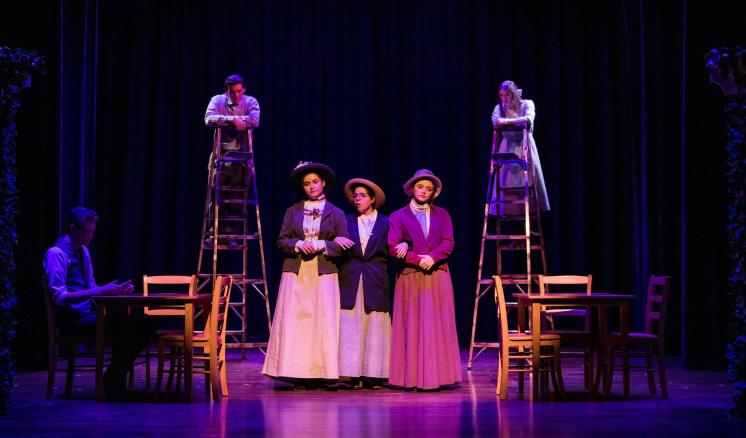 Performers in period costumes on stage with ladders and purple lighting