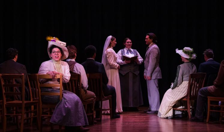 Actors in early 20th-century costumes perform a wedding scene on stage.