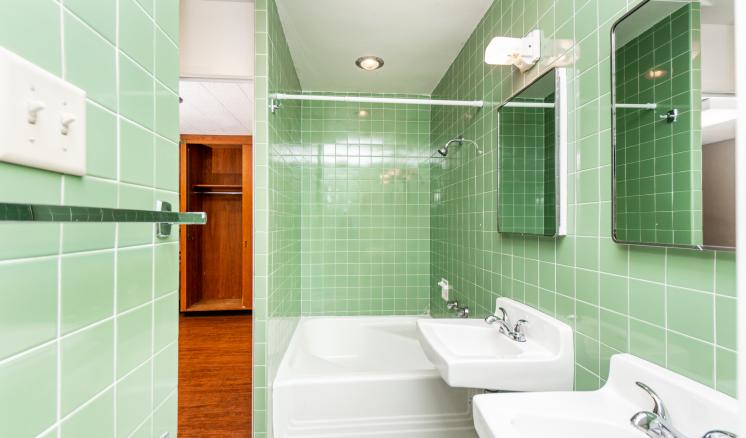 Bathroom with green tile walls, a white bathtub, and a sink with mirrors.