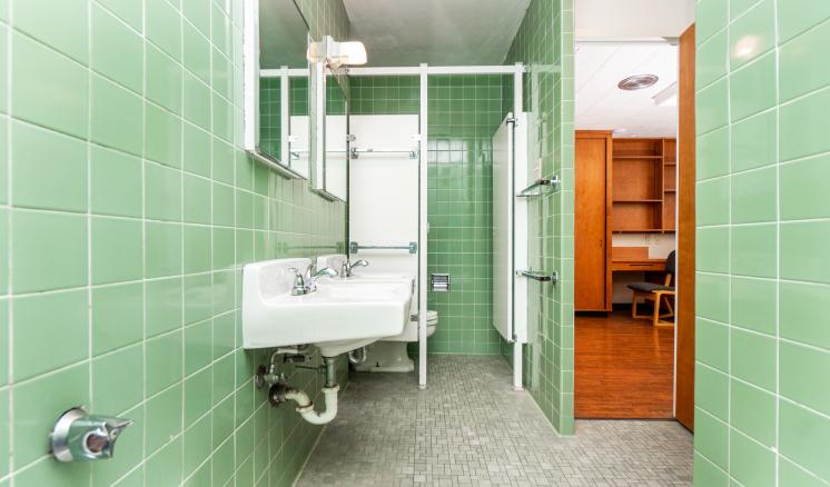 Bathroom with green-tiled walls, a white sink, and an adjacent room visible through an open door.