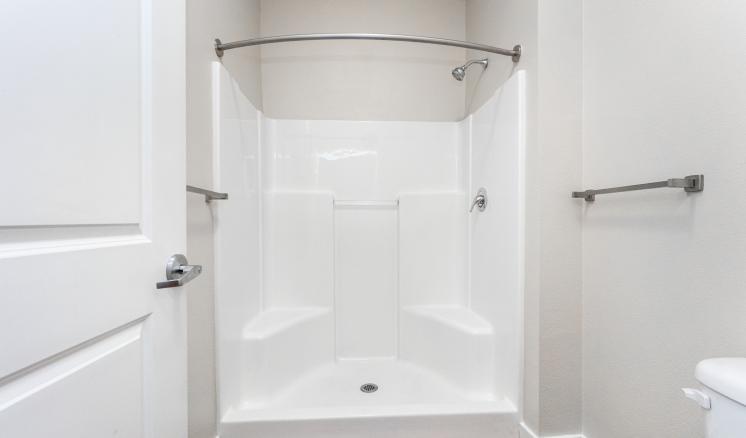 Bathroom with a white shower, silver fixtures, and wooden floor.
