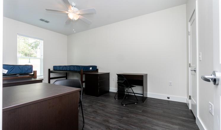 Dormitory room with a bunk bed, desks, and a ceiling fan.