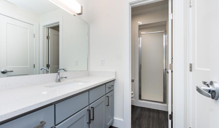 Modern bathroom with a sink, mirror, cabinets, and a shower with a frosted glass door.