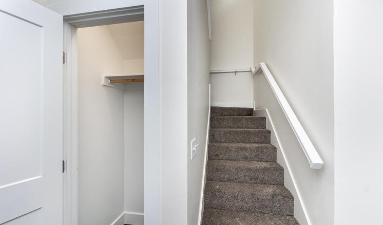Open closet next to a carpeted staircase with a white handrail.