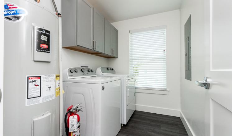 Modern laundry room with washing machine, dryer, cabinets, and a water heater.