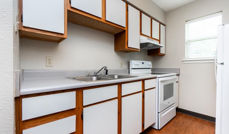 Narrow kitchen with white cabinets, a gray countertop, a stove, a refrigerator, and a fire extinguisher on the wall.
