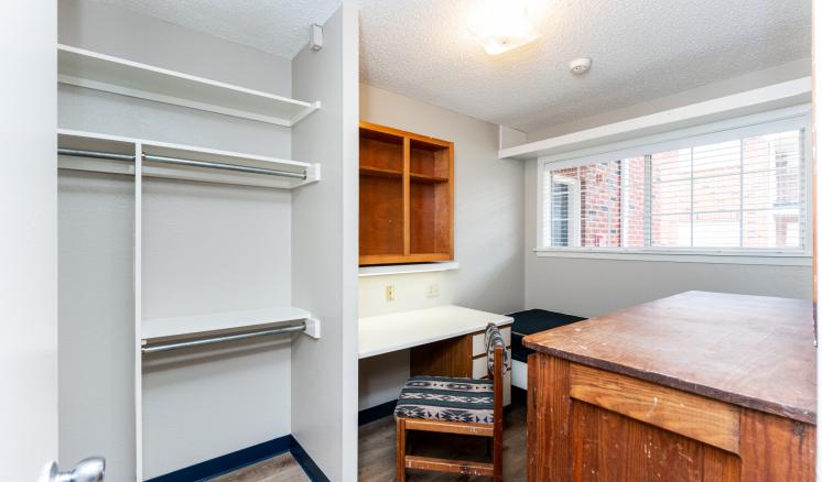 Small unfurnished room with a closet, desk, and window.