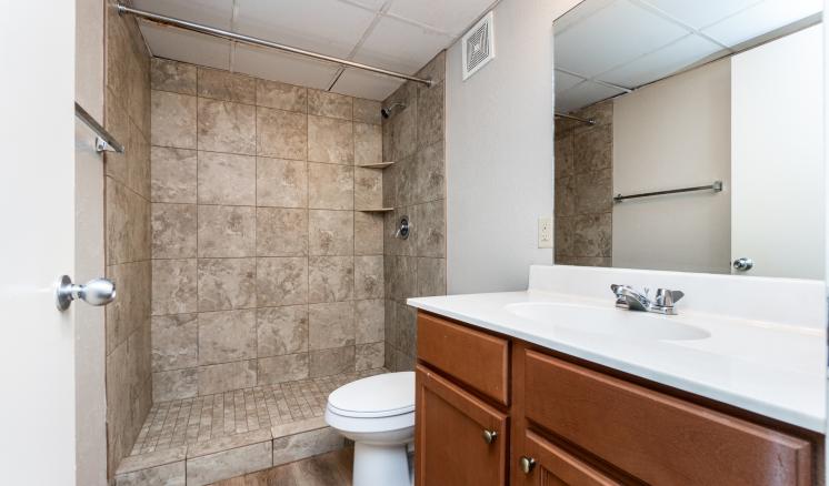 Modern bathroom with tiled shower, toilet, and wooden vanity.