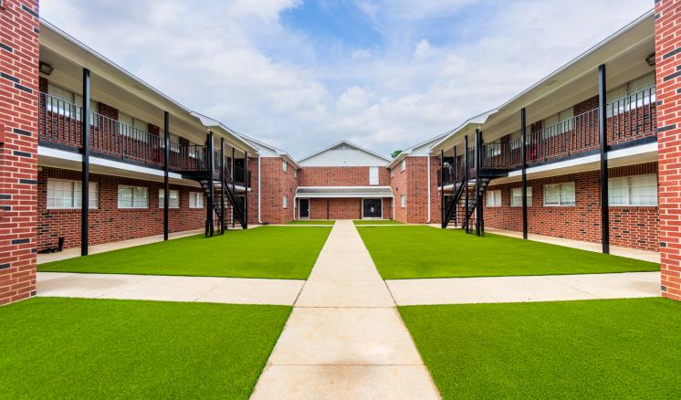 Symmetrical courtyard with red brick buildings and a green lawn intersected by a concrete path.