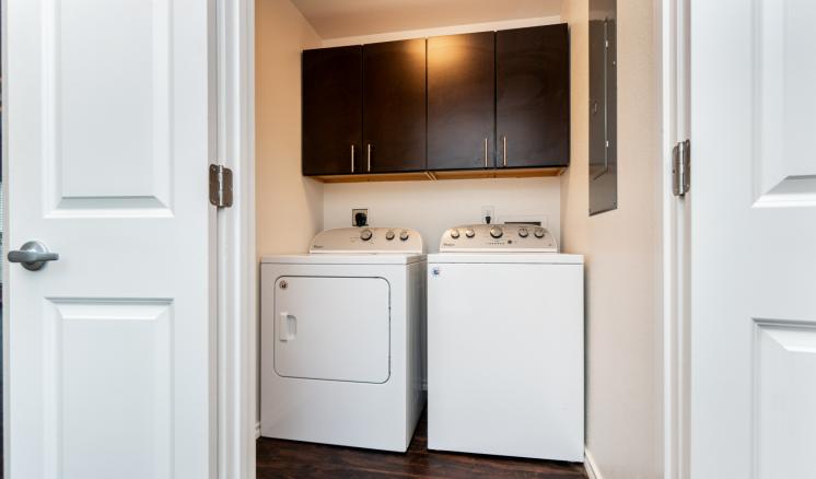 Compact laundry room with a dryer, washing machine, and overhead dark wooden cabinet.