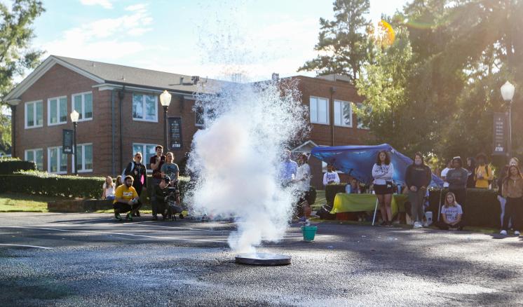A group of people standing on the side of a parking lot with smoke in the middle