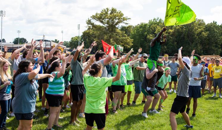 Group of people cheering outdoors with green and red flags raised.
