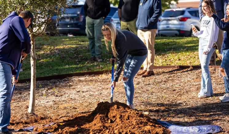 Group of people participating in planting a tree in an outdoor area.
