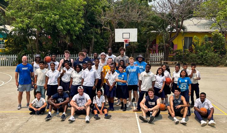 ETBU Men's Basketball Team stand on a basketball court with youth in Honduras