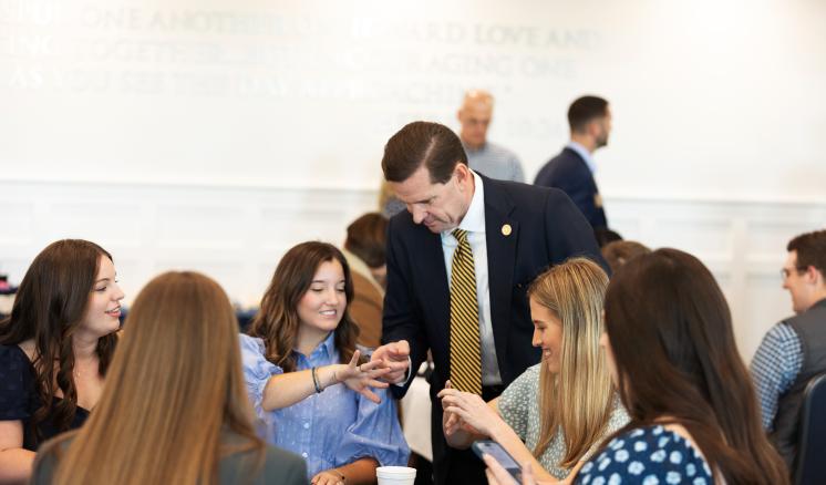 A group of students seated at a table engages with a faculty member during a ring ceremony event.