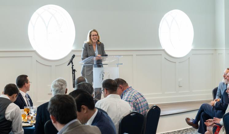 A woman stood in front of a podium speaking to a well lit room of people