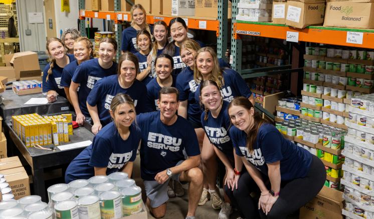 A group of people kneeling for a group photo inside a tightly packed warehouse