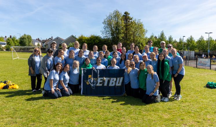A large group of people standing outside in broad daylight with an ETBU banner in front of them