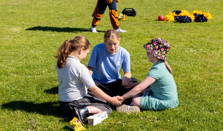 Three children sitting on grass, engaged in an activity on a sunny day.