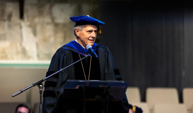 A man speaking behind a podium in academic regalia