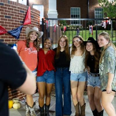 A group of girls in western wearing smiling at a camera outside at night.