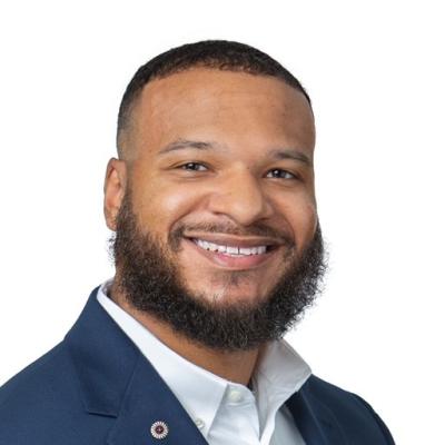 Smiling man with a trimmed beard, wearing a dark blazer over a white shirt.