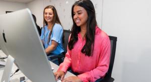 Two female students in a Mac computer lab with grey walls.