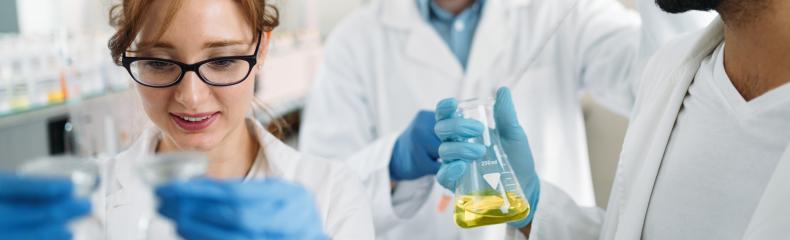 Three researchers in a lab, smiling and holding beakers with substances.