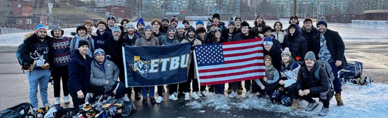 ETBU Hockey team stands in a large group outside in winter gear holding an ETBU branded flag and the American Flag