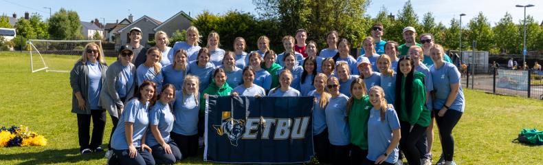 A large group of people standing outside in broad daylight with an ETBU banner in front of them